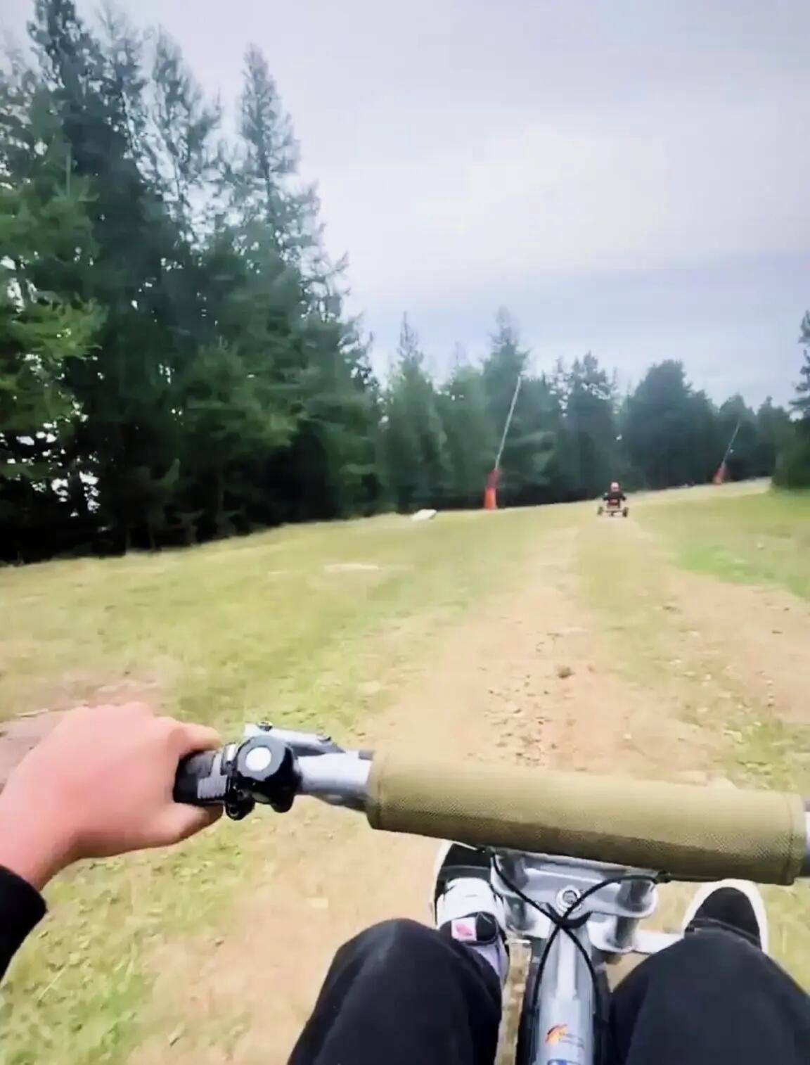 En støvet sti med træer på den ene side, og en person cykler forbi.
