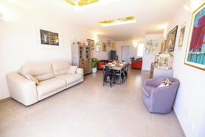 Una sala de estar con sofá, mesa de comedor, sillas, un aparador y una lámpara.