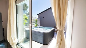Una habitación moderna con puerta de vidrio corredera que da a un balcón, una bañera de hidromasaje y vistas de un edificio.