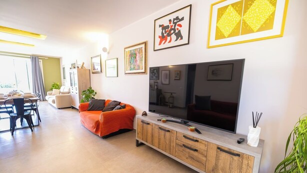 Una sala moderna con un televisor de pantalla plana grande, un sofá, un comedor con mesa y sillas, y una cocina con armarios.