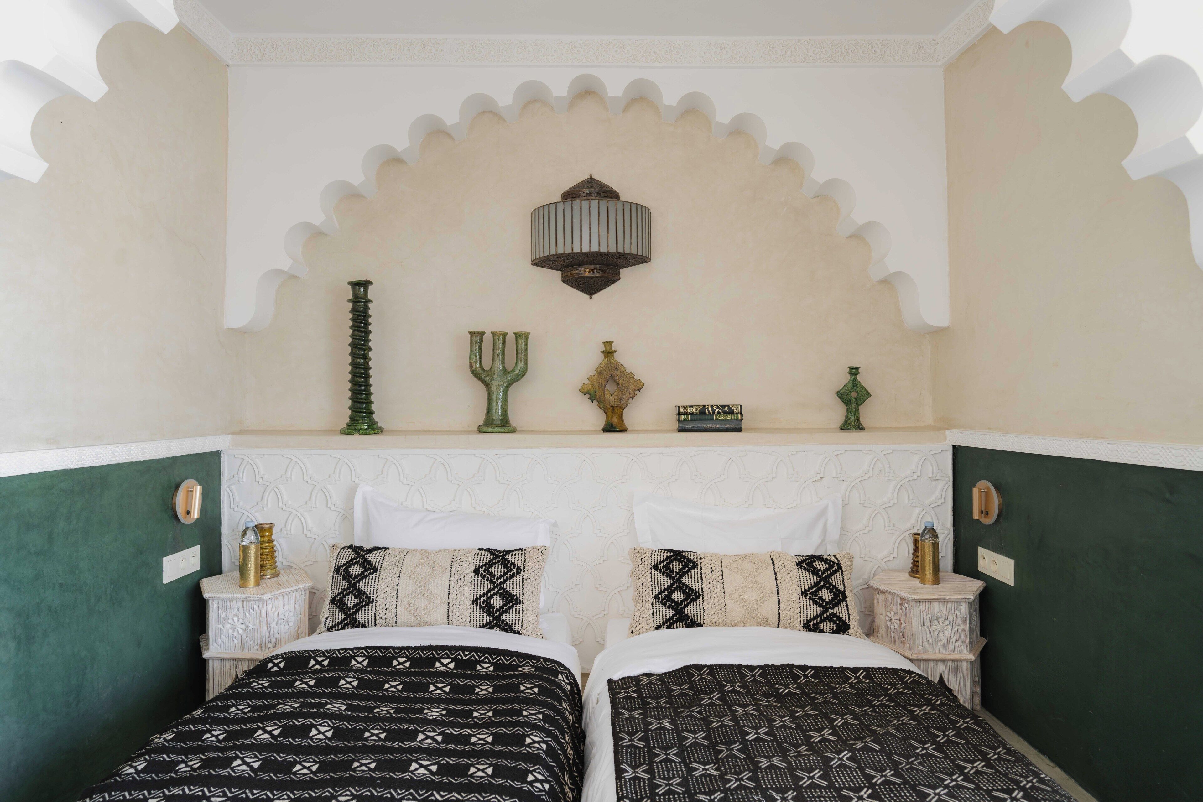 A room with two beds, a decorative wall, and a shelf with various items.