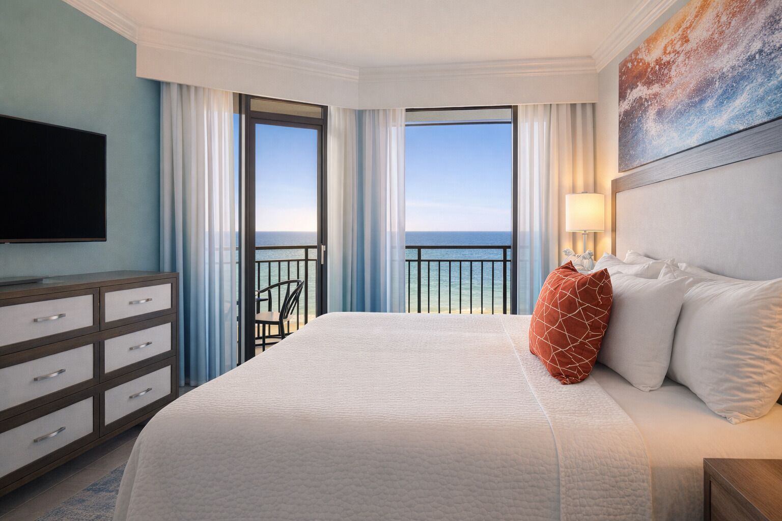 Une chambre d’hôtel avec un lit, une télévision, une commode et un balcon donnant sur l’océan.