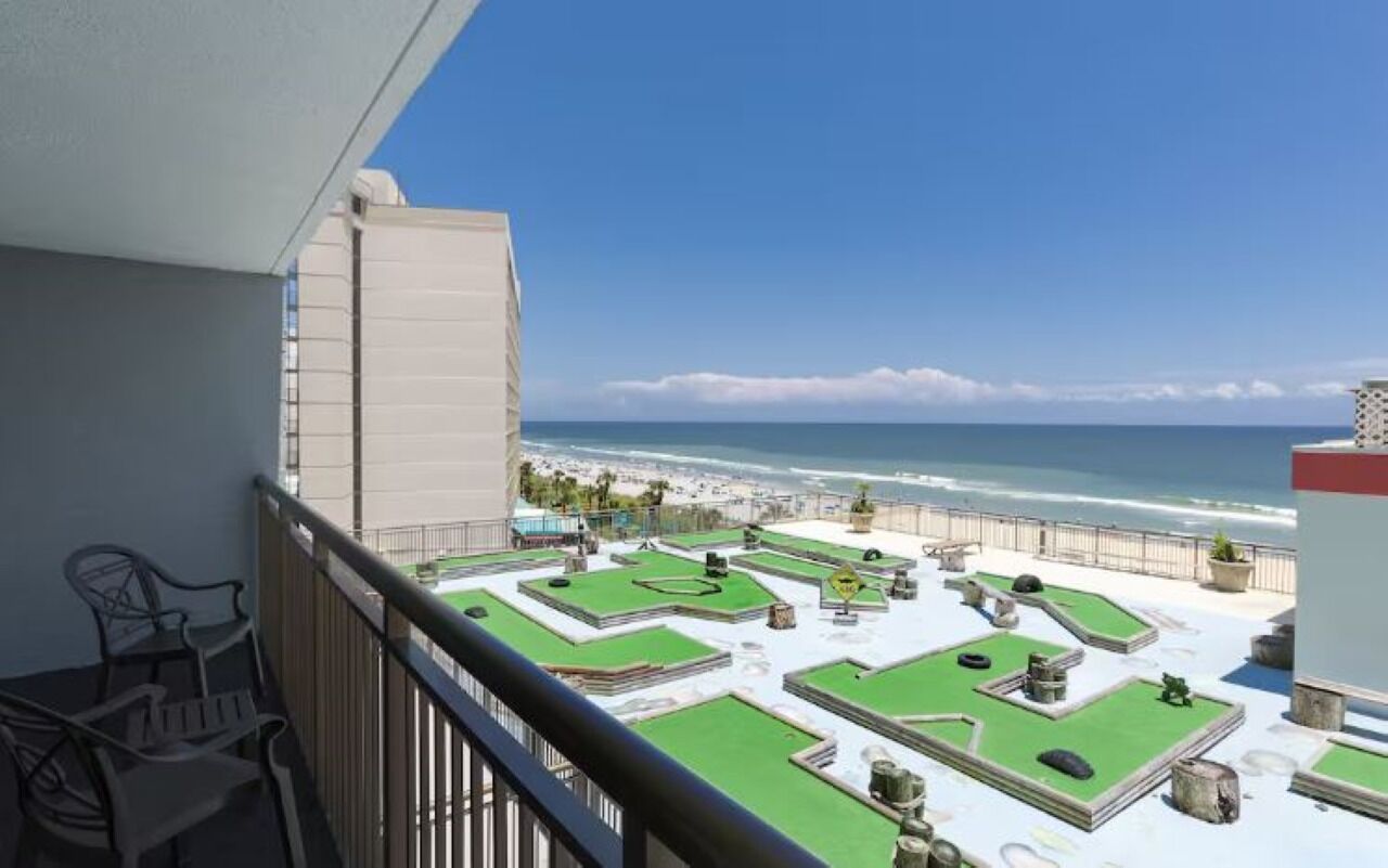 A balcony with a view of the ocean, green artificial turf, and outdoor furniture.