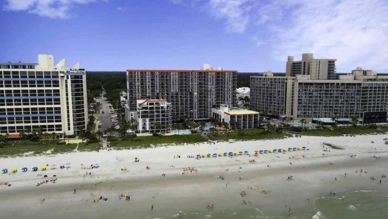 A beachfront hotel with multiple high-rise buildings, a sandy beach, and umbrellas.