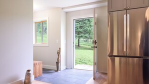Eine moderne Küche mit einem Edelstahl-Kühlschrank, einer Holzbank und Blick auf eine grüne Außenanlage durch eine Glastür.