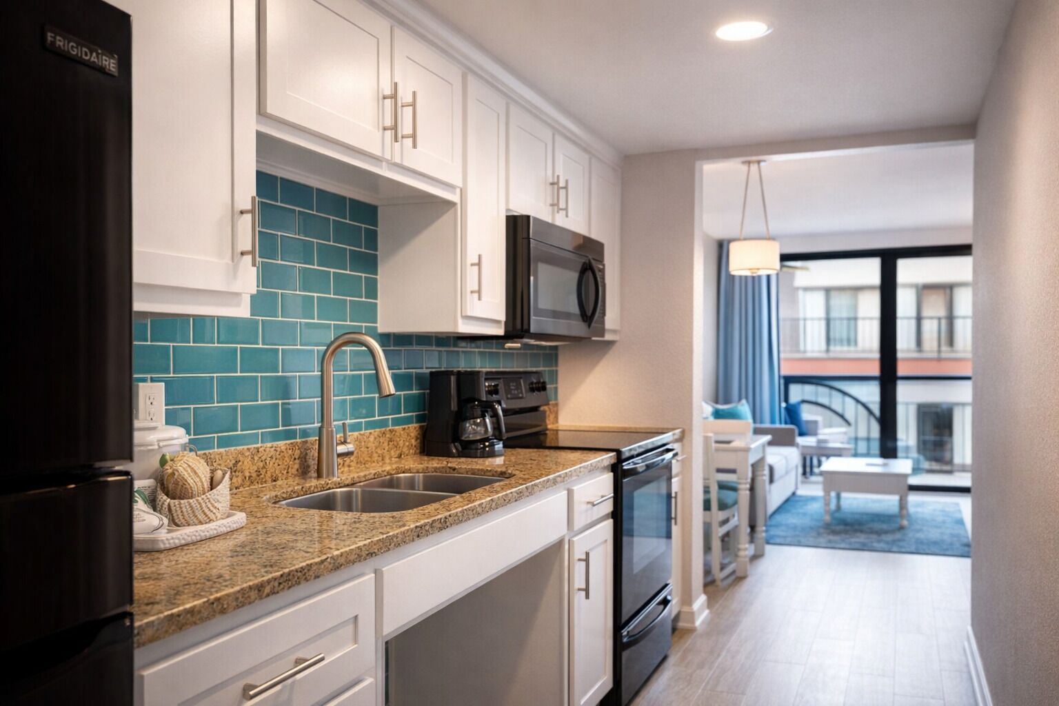 A modern kitchen with white cabinets, a teal backsplash, stainless steel appliances, and a granite countertop.
