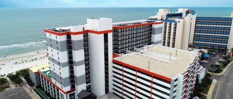 A hotel with multiple floors, a parking area, and a beach view.