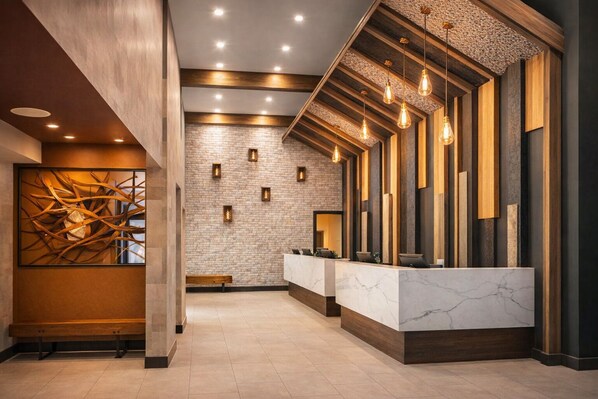 Un espace d’accueil doté d’un comptoir en marbre, de touches décoratives en bois, d’un mur en briques et d’un luminaire moderne.