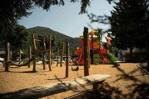 Une aire de jeux avec un toboggan, des structures d’escalade et un espace sablonneux.