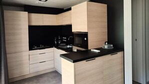 A modern kitchen with light wood cabinetry, a black countertop, and a Bosch microwave. - Chalet SPA Premium 42m² - 2 bedrooms + Covered terrace + Reversible air conditioning + TV 4 people (AX LES THERMES)