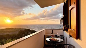 A balcony with a table set for two, a bottle of wine, and a plate of food. The balcony overlooks a coastal landscape with the ocean and a road in the distance. - Casa Caterina - Spacious Sea-View Apart (La Ciaccia)