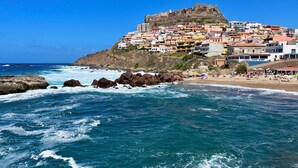 A coastal town with a prominent hilltop fortress, a beach with umbrellas, and rocky coastline. - Casa Caterina - Spacious Sea-View Apart (La Ciaccia)