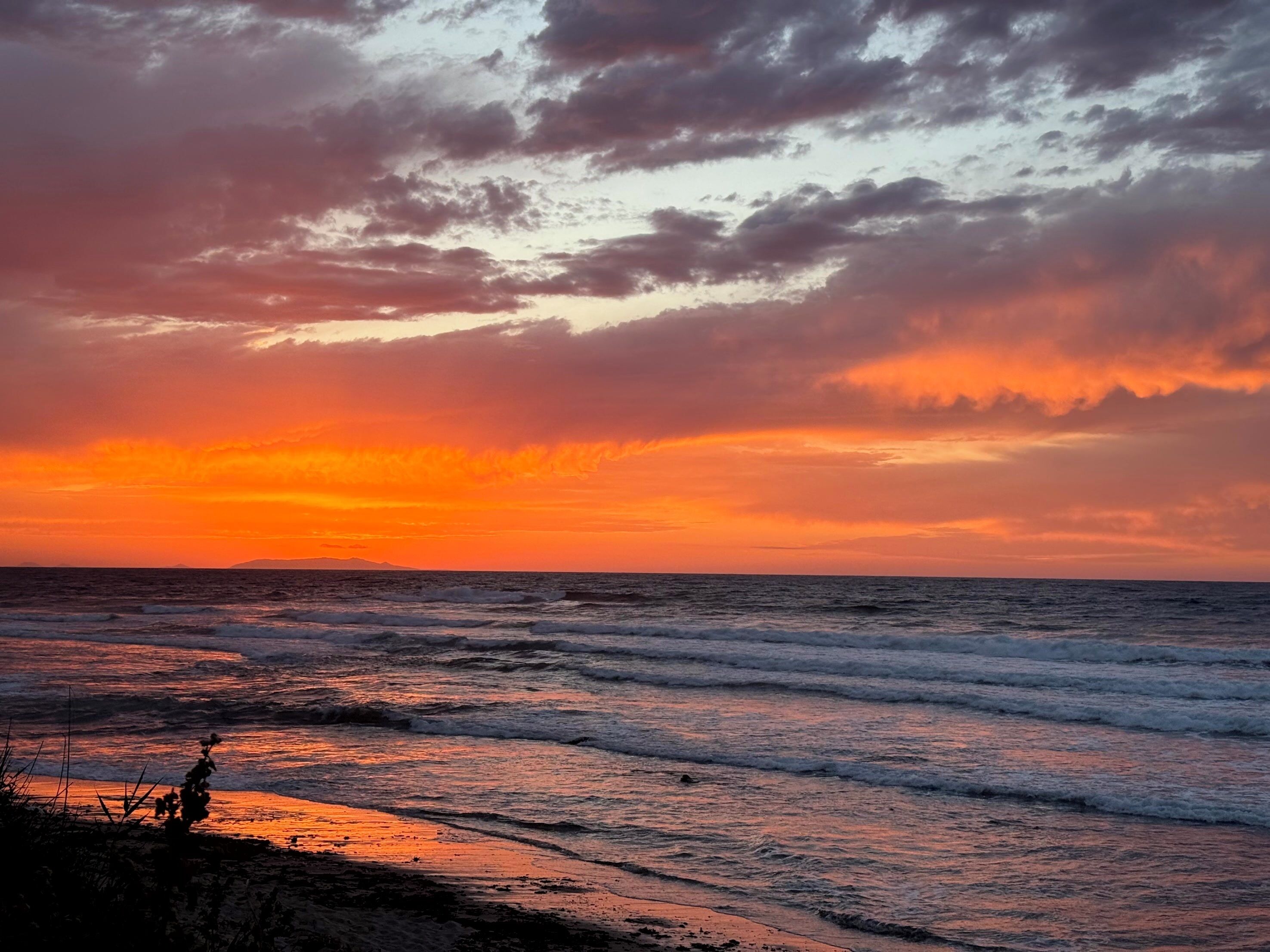 Ein Sonnenuntergang über dem Meer mit Wellen und der Silhouette einer Person.
