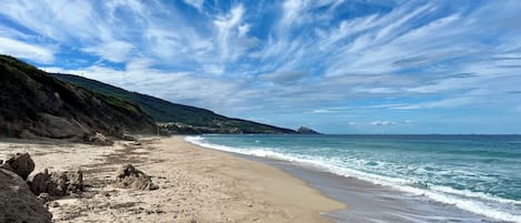 Una spiaggia con cielo sereno, onde calme e un litorale roccioso.