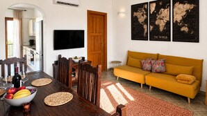 A modern living room with a sofa, a dining table with chairs, a TV, and wall art. - Casa Caterina - Spacious Sea-View Apart (La Ciaccia)