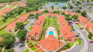 Um bairro residencial com casas de telhados vermelhos, uma piscina central e um lago ao fundo.