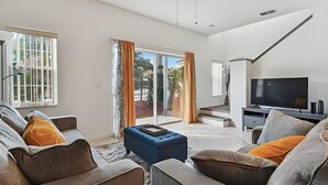Uma sala de estar moderna com um conjunto de sofás, uma televisão e uma escada que leva a uma varanda.