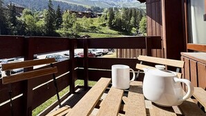 A wooden balcony with a table and chairs, overlooking a mountainous landscape with buildings and trees. - Le Morel 35 - Lovely apartment completely renovated (LES AVANCHERS VALMOREL)