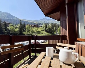 Ein Holzbalkon mit Tisch und Stühlen, mit Blick auf eine gebirgige Landschaft mit Gebäuden und Bäumen.