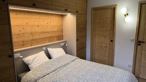 A bedroom with a wooden headboard, a bed with patterned bedding, bedside lamps, and a wooden wardrobe. - Le Morel 35 - Lovely apartment completely renovated (LES AVANCHERS VALMOREL)