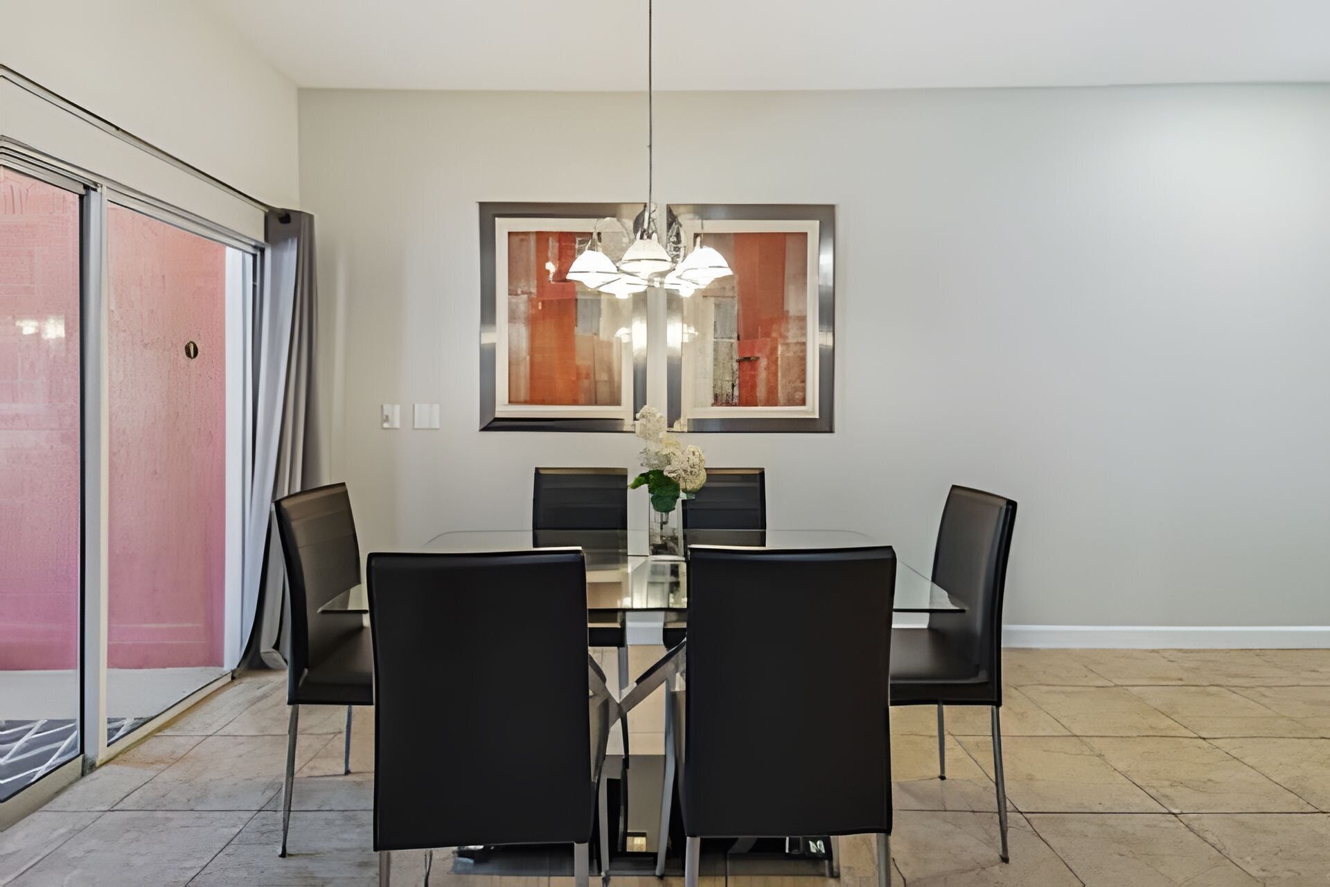 A dining area with a rectangular table, four black chairs, a vase with flowers, and a modern pendant light.
