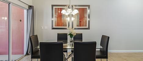 A dining area with a rectangular table, four black chairs, a vase with flowers, and a modern pendant light.