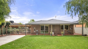 A two-story brick house with a covered patio, a fenced backyard, and a clear sky. - Charming 3-bed Family Home With Amazing Garden (Melbourne)