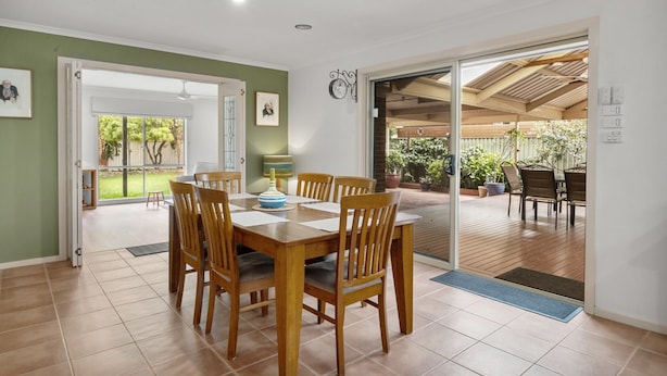 A dining area with a wooden table and chairs, a clock on the wall, and a view of the outdoor patio. - Charming 3-bed Family Home With Amazing Garden (Melbourne)