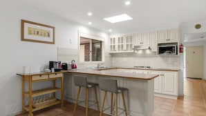A modern kitchen with white cabinets, a wooden island with bar stools, a microwave, and a sink. - Charming 3-bed Family Home With Amazing Garden (Melbourne)