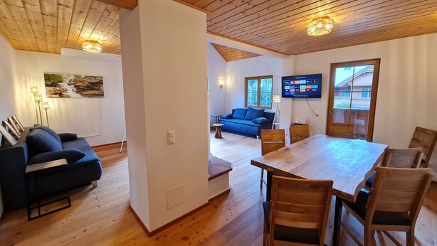 Ein Holzinterieur mit Esstisch, Stühlen, einer Couch und einem an der Wand montierten Fernseher.