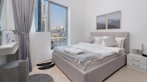 Ein modernes Schlafzimmer mit einem großen Bett, einem Nachttisch, einem Fenster mit Blick auf die Stadt und einem gerahmten Bild an der Wand.