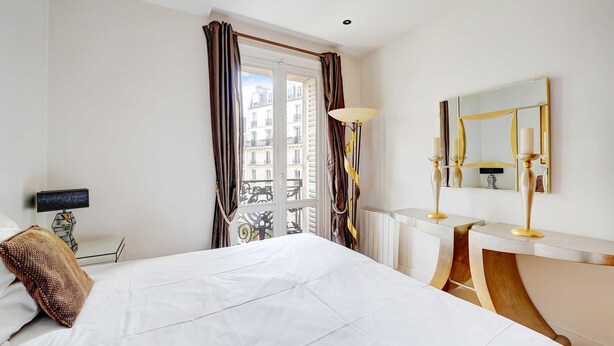 A hotel room with a bed, a bedside table, a lamp, a mirror, and a view of the city through the window. - Bright Apartment - 2br/4p - Muette/passy - Trocadero (Paris)