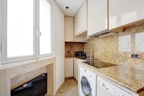 Cocina compacta con lavadora integrada, estufa y ventana.