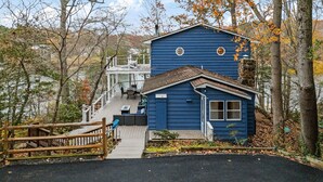 Une cabane bleue avec un porche et une cheminée en pierre, entourée d’arbres et d’une clôture en bois.