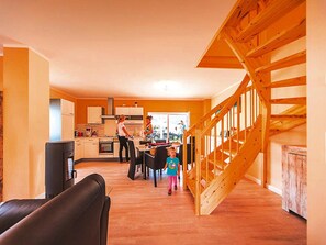 A modern kitchen with white cabinets, a wooden staircase, and a dining area with a black leather couch. - Ferienhaus Hyggelig in Seehausen am Oberuckerse (Oberuckersee)