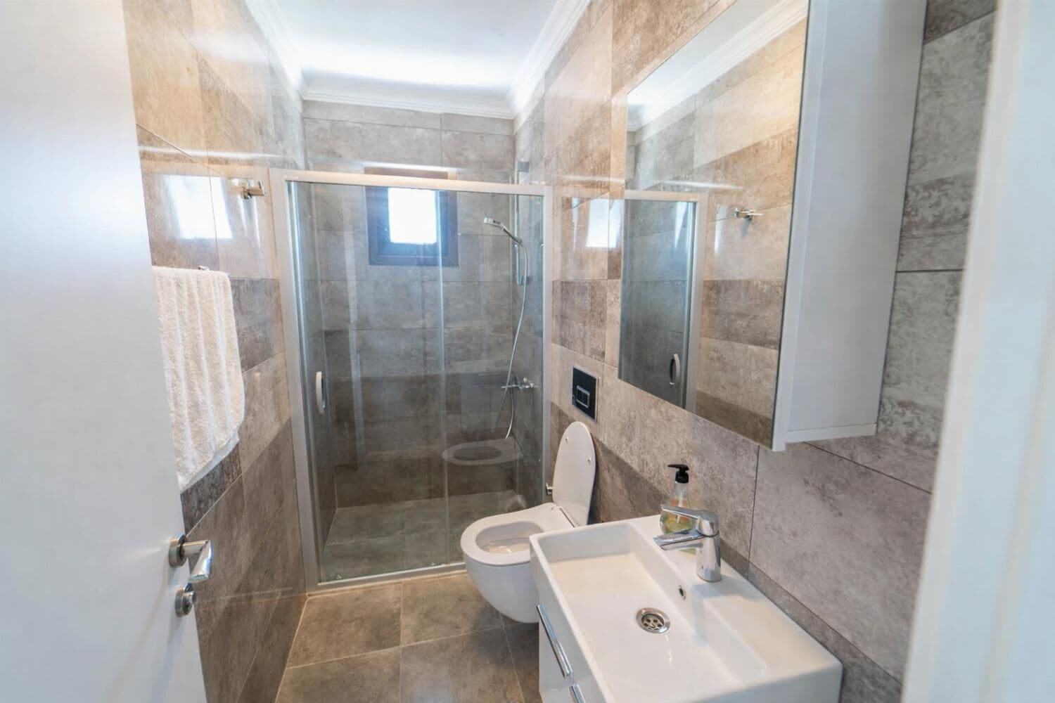 Een badkamer met een douchecabine van glas, toilet, wastafel en spiegel.