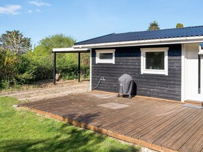 A wooden deck leading to a dark-colored building with a covered grill area, a small window, and a covered outdoor seating area. - 4 Star Holiday Home in Slagelse (Slagelse)