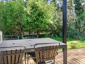 An outdoor wooden deck with a table and chairs, surrounded by dense greenery. - 4 Star Holiday Home in Slagelse (Slagelse)