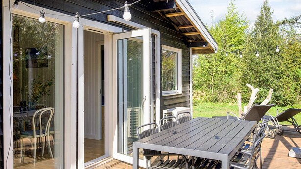 An outdoor deck with a table and chairs, a sliding glass door, and a wooden deck. - 4 Star Holiday Home in Slagelse (Slagelse)