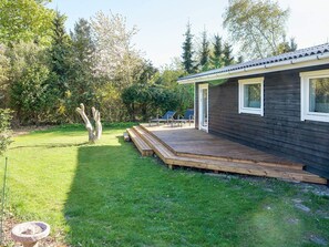 A wooden deck leading to a dark-colored building with a window, surrounded by a grassy yard and trees. - 4 Star Holiday Home in Slagelse (Slagelse)
