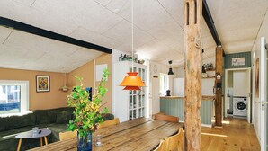 A cozy living room with a wooden dining table, a sofa, and a coffee table. There is a kitchen area in the background with a washing machine. - 4 Star Holiday Home in Slagelse (Slagelse)
