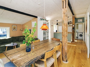 A cozy living room with a wooden dining table, a sofa, and a coffee table. There is a kitchen area in the background with a washing machine. - 4 Star Holiday Home in Slagelse (Slagelse)