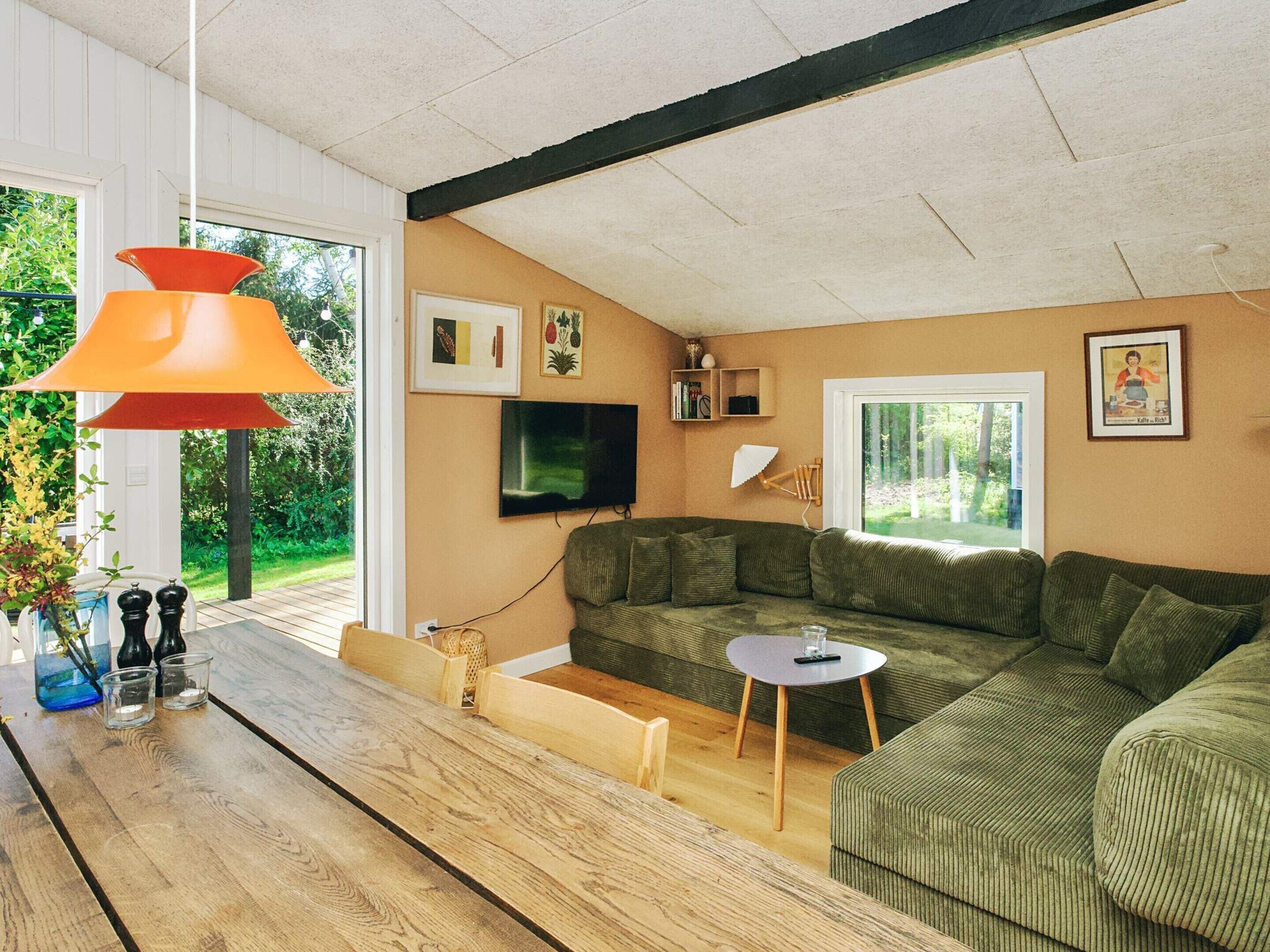 Uma sala de estar moderna com sofá seccional, mesa de centro de madeira, televisão e uma janela grande.