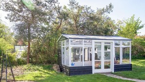 A conservatory with a glass roof, surrounded by a garden with a brick path and trees. - 4 Star Holiday Home in Slagelse (Slagelse)