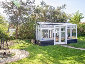 A conservatory with a glass roof, surrounded by a garden with a brick path and trees. - 4 Star Holiday Home in Slagelse (Slagelse)