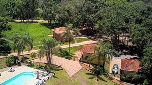 Il s’agit d’une propriété résidentielle dotée d’une piscine, d’une terrasse dallée et d’un bâtiment à toit rouge, le tout entouré d’une végétation luxuriante.