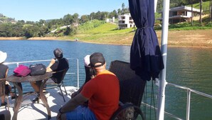 Un bateau doté d’un espace extérieur avec des sièges et une table, entouré d’eau et de verdure.