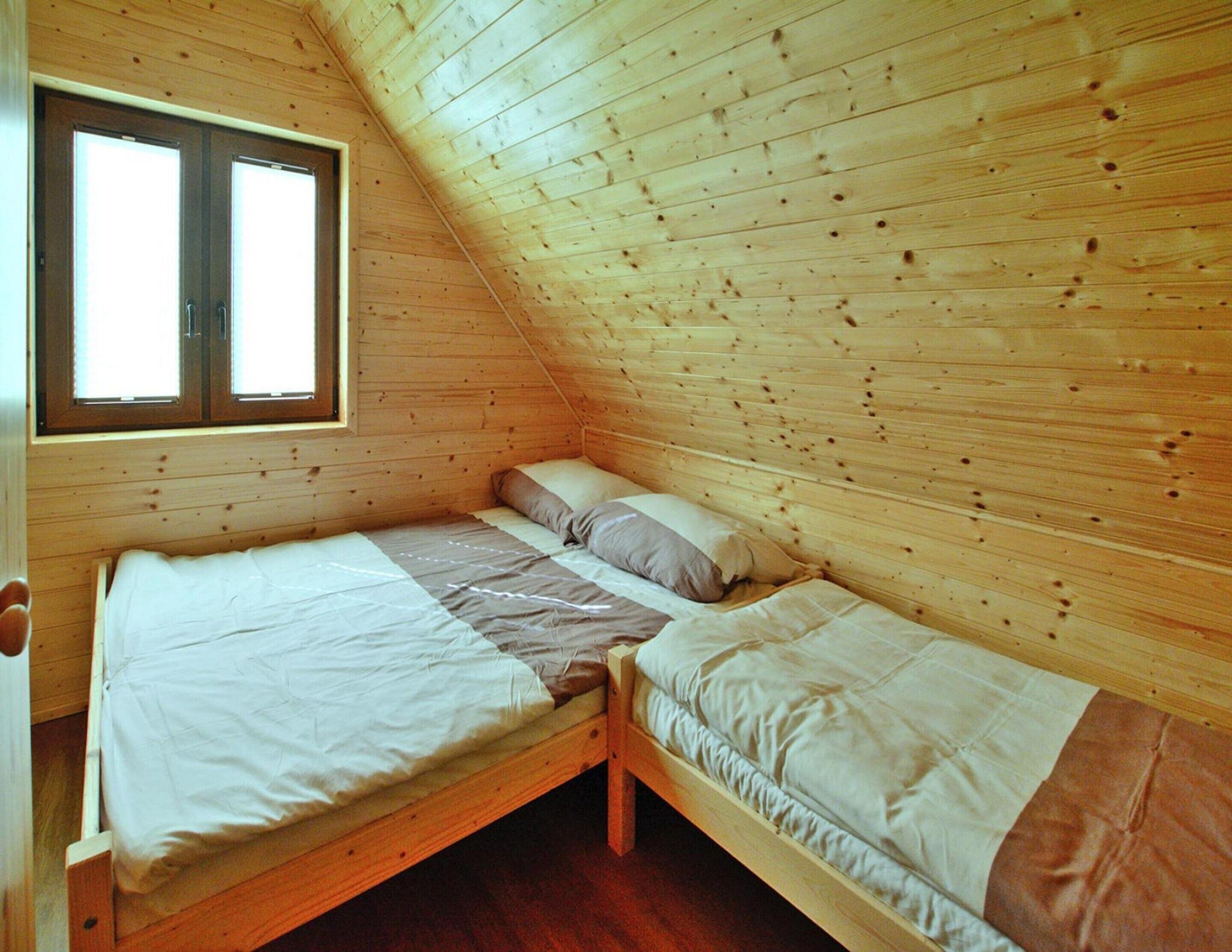 A small, wooden-paneled room with two single beds, a window, and a sloped ceiling.