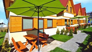 Una casa de madera con techo rojo, asientos exteriores y un paraguas verde.