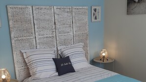 Ein ordentlich bezogenes Bett mit gestreifter Bettwäsche und einer blauen Decke, ein gewebter Kopfteil, Nachttischlampen und ein kleiner Teppich.